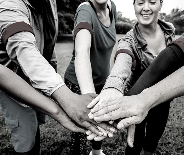 group of people in semi-circle with hands in the center on top of each other