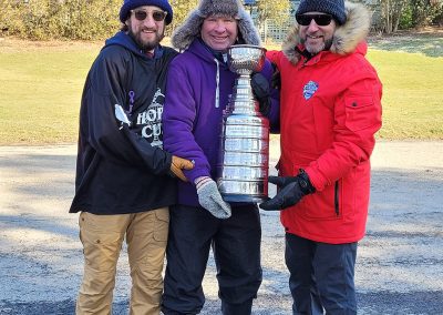three men in winter clothes hold a trophy cup