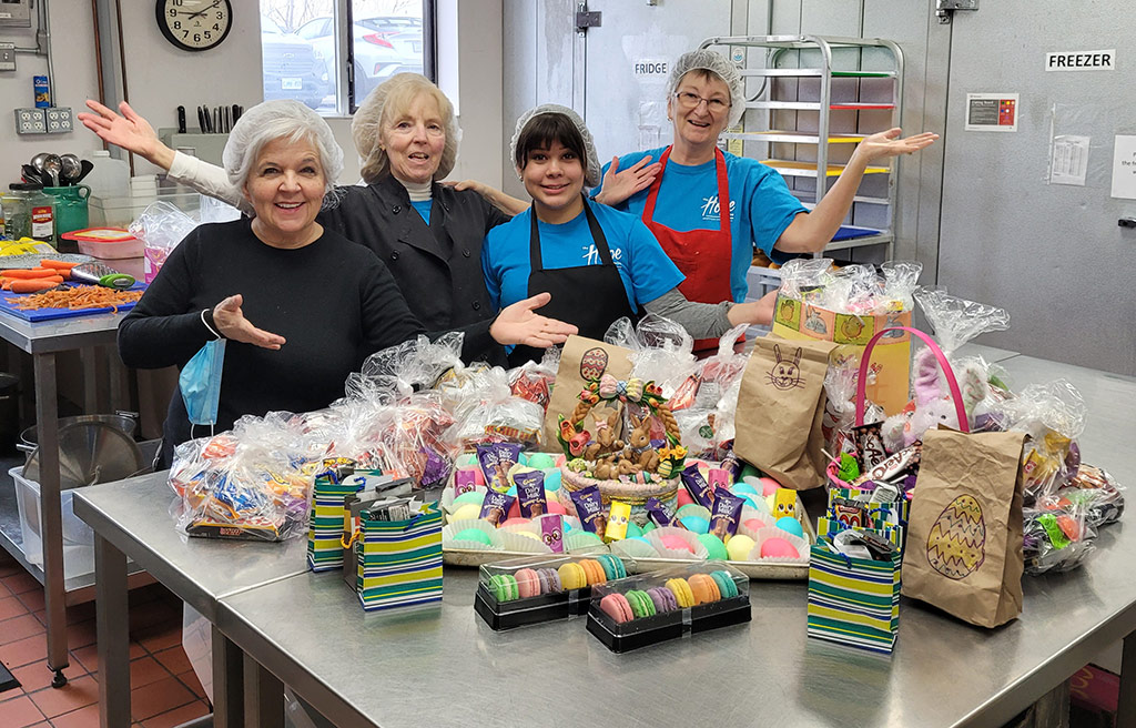 volunteers pose in kitchen in front of prepared food for the community lunch